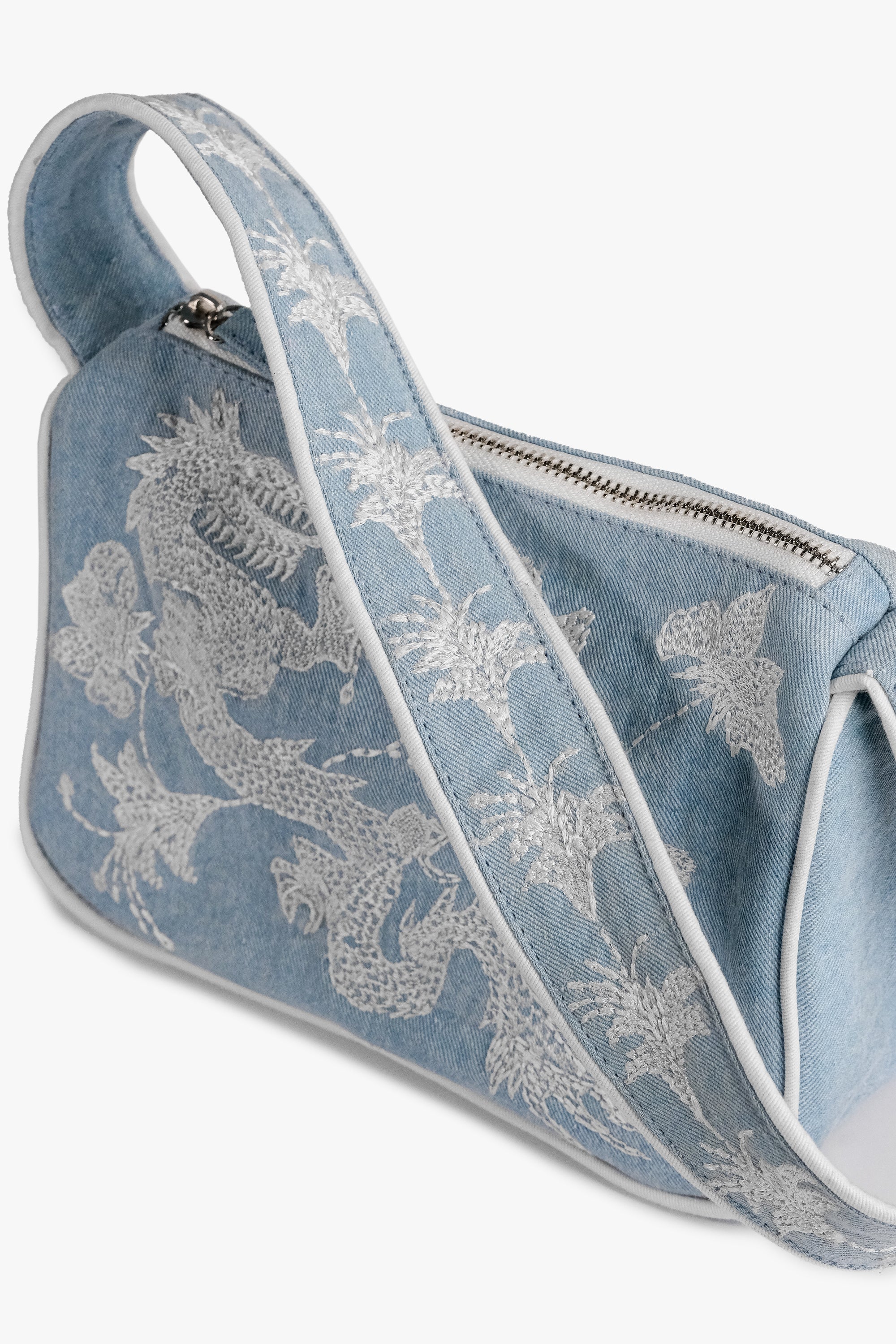 Acambha's Embroidered Dragon & Flowers Shoulder Bag with intricate embroidery of a dragon and flowers on light denim. Features a zipper closure and white embroidery on the body and strap