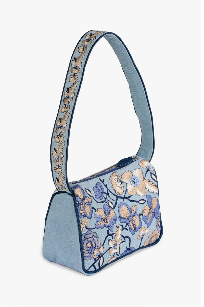 Acambha's Embroidered Denim Shoulder Bag, featuring multi-colored embroidery on light denim. Meticulous craftsmanship, extending from the body to the strap. Framed with dark blue piping.