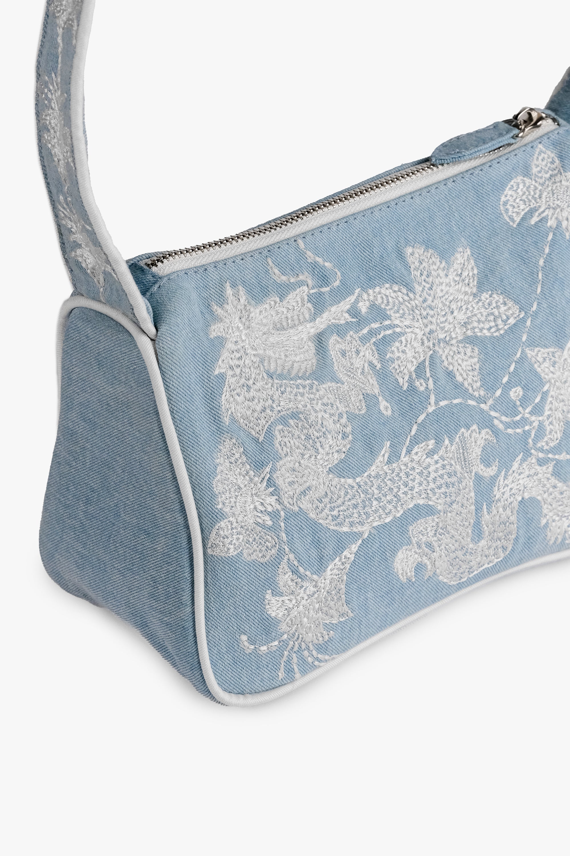 Acambha's Embroidered Dragon & Flowers Shoulder Bag with intricate embroidery of a dragon and flowers on light denim. Features a zipper closure and white embroidery on the body and strap